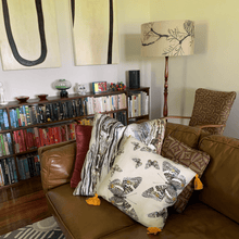 Load image into Gallery viewer, soft paperbark and butterflies in grey, yellow and beige neutrals printed on square linen designer cushions on a leather lounge with book case and contemporary Australiana decore