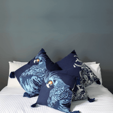Load image into Gallery viewer, Black cockatoo and sage grevillea printed on indigo square linen designer cushion with tassels on white sheets on bed in bedroom with charcole walls