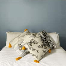 Load image into Gallery viewer, Butterfly print in grey, yellow and beige neutrals printed on square linen designer handmade cushion on bed with white sheets in light bedroom