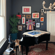 Load image into Gallery viewer, A picture of a Dark living room with Indigenous Australian Art on a baby grand piano and monstera in a pot