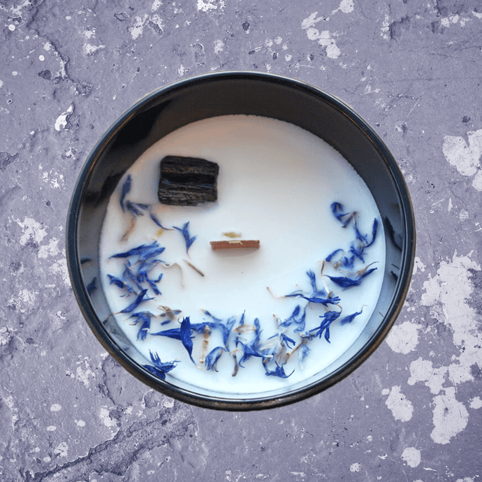 A picture of a large white candle sprinkled with Cornflower petals and a  Black tourmaline crystal imbedded in it