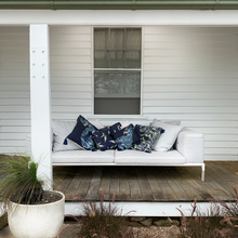 Load image into Gallery viewer, Black cockatoo and sage grevillea printed on indigo square linen designer cushion with tassels on white sheets on outdoor lounge on victorian farmhouse veranda
