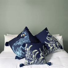 Load image into Gallery viewer, Black cockatoo and sage grevillea printed on indigo square linen designer cushion with tassels on white sheets on bed in bedroom with sage walls 
